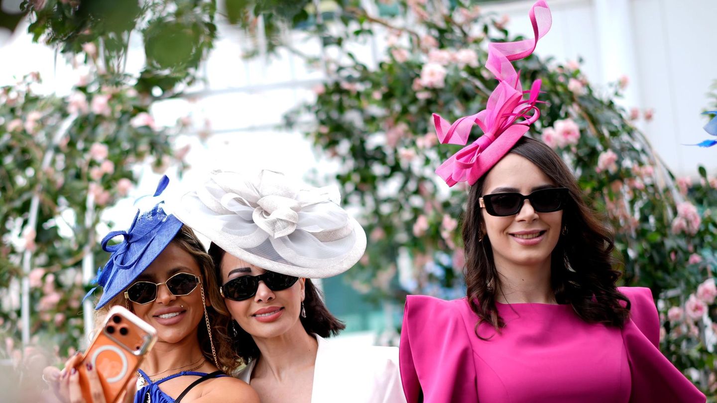 Epsom, Großbritannien. Rennbesucherinnen mit extravaganter Kopfbedeckung machen ein Selfie am „Ladies Day“ des Betfred-Derby-Festivals auf der Epsom Downs Rennbahn.