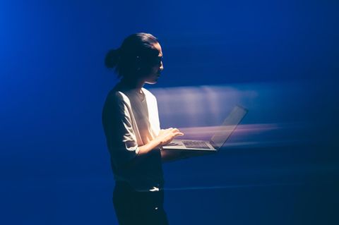 Ein Mann mit einem Laptop steht vor einem blauen Hintergrund