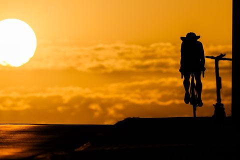 Ein Fahrradfahrer fährt bei Sonnenaufgang über eine Brücke in der Region Hannover. Hitze ist besonders am Nachmittag gefährlich.