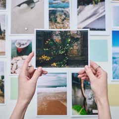 Hände halten ein gedrucktes Foto hoch, im Hintergrund hängen Fotos an der Wand