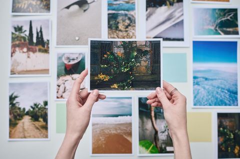 Hände halten ein gedrucktes Foto hoch, im Hintergrund hängen Fotos an der Wand