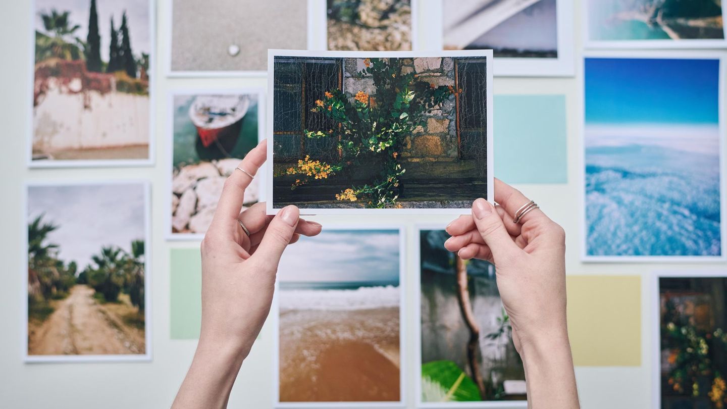 Hände halten ein gedrucktes Foto hoch, im Hintergrund hängen Fotos an der Wand
