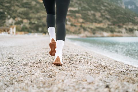 Eine Frau läuft in weißen Adidas-Socken am Strand entlang
