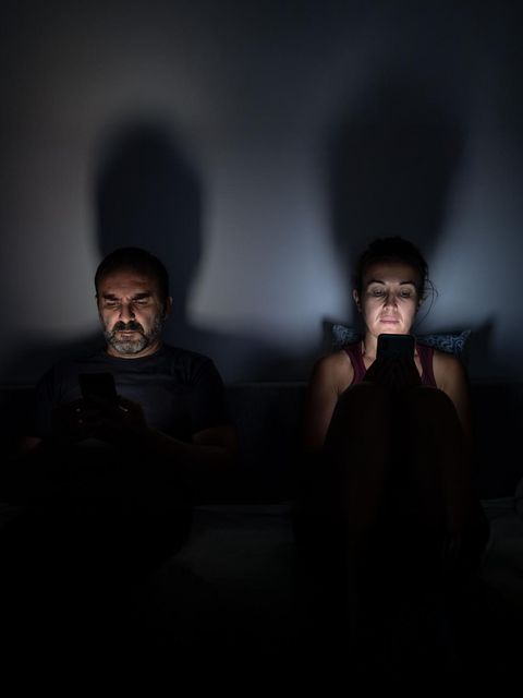 Ein Paar sitzt im Bett und schaut aufs Handy (Symbolbild Beziehungskrise)