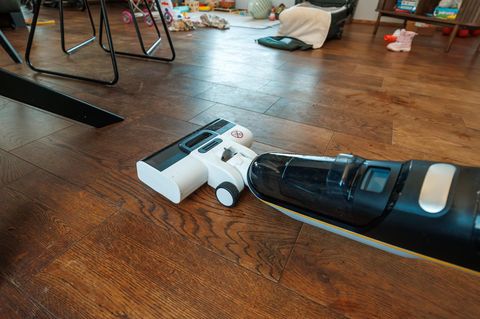 Ein kabelloser Nass-Trockenstaubsauger reinigt den dunklen Holzboden im Familienzimmer
