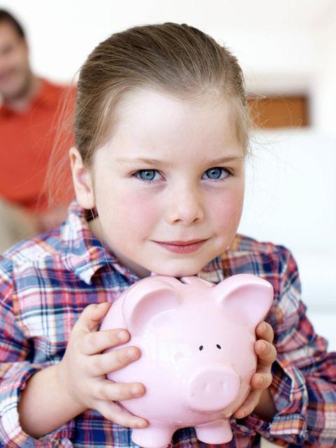 Ein Mädchen hält ein Sparschwein in der Hand, hinter ihr sitzt ein lächelndes Paar.