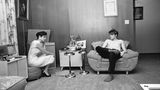 In seinem Wohnzimmer in Memphis hört sich der Sänger knapp bekleidet und ganz entspannt die Aufnahmen für seine Hitsingle "Hound Dog" und "Don't Be Cruel" an, die er am 13. Juli 1956 veröffentlichte. Die Dame ist seine damalige Freundin Barbara Hearn.  Das Foto entstammt dem Bildband "Alfred Wertheimer. Elvis and the Birth of Rock and Roll" (Taschen Verlag)
