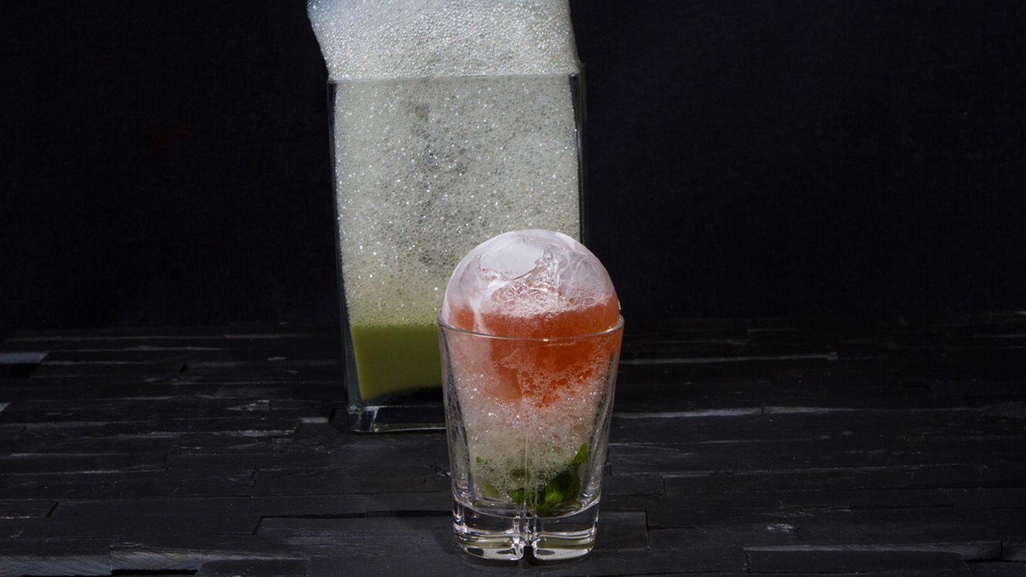Present Cocktail  Wie verpackt ein Bartender ein Geschenk? Richtig, in einer Eiskugel! Ob Sie Ihren Gästen einen Löffel zur Verfügung stellen, um das "Auspacken" zu erleichtern, bleibt Ihnen überlassen. Denn nach einer Weile sorgt das Schmelzen der Kugel auch von ganz allein dafür, dass die Zutaten zueinander finden.  Zutaten:  50ml Grappa  15ml frisch gepresster Zitronensaft  30ml Vanille-Rhabarber-Saft*  Verbenaschaum**  Trinkgefäß: Tumbler  Zubereitung:  Füllen Sie einen Luftballon mit Wasser, sodass der Ballon noch in Ihr Glas passt. Frieren Sie den Luftballon für ca. 3 Stunden und 15 Minuten bei -23°C ein. Nach Ablauf der Zeit schneiden Sie den Luftballon auf und legen Sie die halbgefrorene Eiskugel frei. Schlagen (oder bohren) Sie vorsichtig ein kleines Loch in die Eiskugel und gießen das darin eingeschlossene Wasser aus der Kugel. Legen Sie die Kugel wieder vorsichtig in den Gefrierschrank.  Schütteln Sie nun alle Zutaten abgesehen vom Verbenaschaum mit Eiswürfeln kräftig im Shaker. Geben Sie den Schaum unten ins Glas und setzen Sie darauf die Eiskugel. Füllen Sie die Kugel durch einen Trichter mit dem Drink.  *Schneiden Sie 4 Stangen Rhabarber in kleine Stücke und 2 Vanilleschoten der Länge nach auf. Geben Sie beides mit 50g Zucker in einen Vakuumbeutel. Den Vakuumbeutel verschließen und bei 58 °C für 1 Stunde in ein Wasserbad legen. Den Inhalt des Beutels danach in einen Entsafter geben, um den Saftertrag zu erhöhen.  **Pürieren Sie 1 Bund Verbene mit 50ml frisch gepresstem Zitronensaft, 35ml Läuterzucker, etwas Salz und Pfeffer in ½ Liter Wasser. Passieren Sie anschließend das Gemisch zweimal. Geben Sie 200 ml des Verbenawassers und 2,5g Lecithin in den Mixer. Mit einem Aquariumsprudler wird das Verbena-Lecithin-Wasser zu einem luftigen Schaum aufgeschäumt.