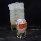 Present Cocktail  Wie verpackt ein Bartender ein Geschenk? Richtig, in einer Eiskugel! Ob Sie Ihren Gästen einen Löffel zur Verfügung stellen, um das "Auspacken" zu erleichtern, bleibt Ihnen überlassen. Denn nach einer Weile sorgt das Schmelzen der Kugel auch von ganz allein dafür, dass die Zutaten zueinander finden.  Zutaten:  50ml Grappa  15ml frisch gepresster Zitronensaft  30ml Vanille-Rhabarber-Saft*  Verbenaschaum**  Trinkgefäß: Tumbler  Zubereitung:  Füllen Sie einen Luftballon mit Wasser, sodass der Ballon noch in Ihr Glas passt. Frieren Sie den Luftballon für ca. 3 Stunden und 15 Minuten bei -23°C ein. Nach Ablauf der Zeit schneiden Sie den Luftballon auf und legen Sie die halbgefrorene Eiskugel frei. Schlagen (oder bohren) Sie vorsichtig ein kleines Loch in die Eiskugel und gießen das darin eingeschlossene Wasser aus der Kugel. Legen Sie die Kugel wieder vorsichtig in den Gefrierschrank.  Schütteln Sie nun alle Zutaten abgesehen vom Verbenaschaum mit Eiswürfeln kräftig im Shaker. Geben Sie den Schaum unten ins Glas und setzen Sie darauf die Eiskugel. Füllen Sie die Kugel durch einen Trichter mit dem Drink.  *Schneiden Sie 4 Stangen Rhabarber in kleine Stücke und 2 Vanilleschoten der Länge nach auf. Geben Sie beides mit 50g Zucker in einen Vakuumbeutel. Den Vakuumbeutel verschließen und bei 58 °C für 1 Stunde in ein Wasserbad legen. Den Inhalt des Beutels danach in einen Entsafter geben, um den Saftertrag zu erhöhen.  **Pürieren Sie 1 Bund Verbene mit 50ml frisch gepresstem Zitronensaft, 35ml Läuterzucker, etwas Salz und Pfeffer in ½ Liter Wasser. Passieren Sie anschließend das Gemisch zweimal. Geben Sie 200 ml des Verbenawassers und 2,5g Lecithin in den Mixer. Mit einem Aquariumsprudler wird das Verbena-Lecithin-Wasser zu einem luftigen Schaum aufgeschäumt.