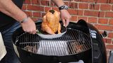 Frisch angemalt und mit Kräutern versehen kommt das Huhn samt Sitz auf den Grill. Die Holzkohlen liegen links und rechts, die Mitte bleibt frei.
