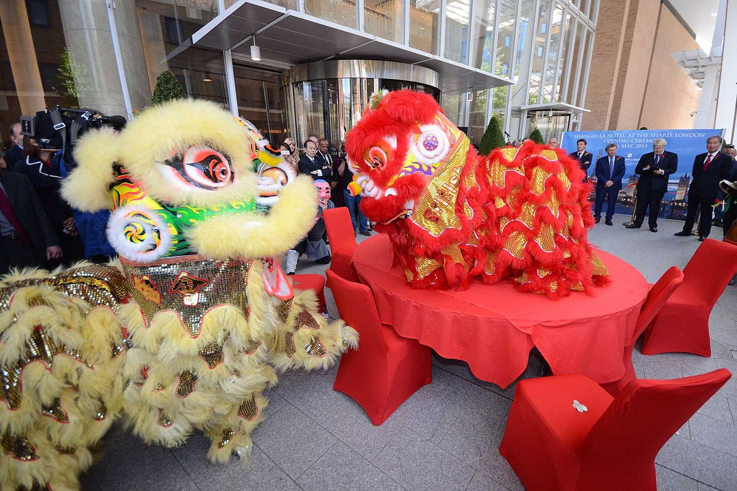 Chinesisches Eröffnungszeremonie vor dem Eingang: Zwei Löwen tanzen erst um und später auf einem runden Tisch. Dann verspeisen die Monster kleine Haufen von Silbermünzen und einen grünen Salatkopf – ein Ritual, das Glück und Wohlstand verspricht.