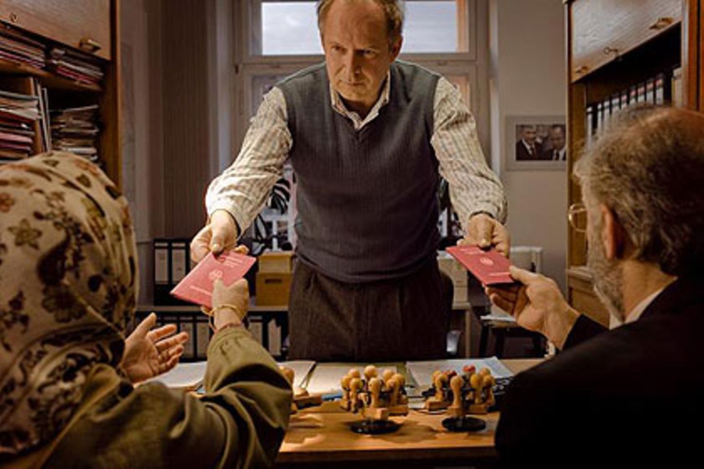 Der Einwanderungsbeamte (Axel Milberg) überreicht zwei eingewanderten Neubürgern ihre deutschen Pässe - und ermahnt sie, immer schön sonntags den "Tatort" zu gucken