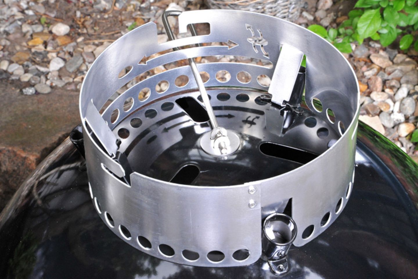Ein Blick auf den umgedrehten Grill. Der Hebel bewegt die Lüftungslamellen und dient zugleich zum Auskehren der Holzkohlenasche. Durch die länglichen Öffnungen der Grillschale zieht später die heiße Holzkohle Luft von außen an. Es entsteht ein Kaminzugeffekt. Je mehr Luft nachströhmt desto heißer brennt die Kohle – desto schneller ist sie jedoch auch verbraucht.