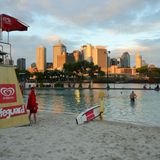 Badestrand in der Stadt: South Bank  In welcher australischen Metropole kann man abends zum Sonnenuntergang durch den Sand stapfen und eine Runde schwimmen? Das geht nur in Brisbane, wo ein brachliegendes Industriegelände in ein begrüntes Freizeitareal umgewandelt wurde - mit Flaniermeile, Palmenwald und Wasserspielen. Zu den South Bank Parklands gehören auch Grillplätze, Dutzende von Restaurants und ein künstliches Wasserbecken mit Badestrand und Lifeguards. Dahinter fließt der Brisbane River Richtung Meer. Die Skyline von Downtown ragt in die Abendhimmel.  www.visitsouthbank.com.au