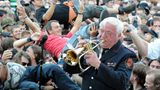Trompete statt Gitarrenriffs: Die Wacken Firefighters, die Blaskapelle der örtlichen Feuerwehr, spielen zum Festival-Auftakt im Biergarten Volkslieder und Adaptionen bekannter Songs. Im Hintergrund verwandelt sich die tobsüchtige Meute in ein betrunkenes, schunkelndes Menschenmeer.