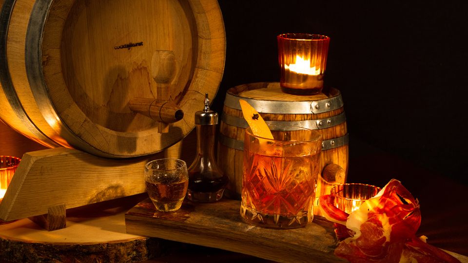 Stephan Hinz: Bacon & Barrel Old Fashioned Wer schon einmal ein ordentliches Barbecue erlebt hat, der weiß, wie sehr gutes Fleisch und kräftiger Bourbon harmonieren. Klar, dass dieses klassisch amerikanische Ritual sich auch in einem klassisch amerikanischen Drink einfangen lässt – dem Old Fashioned. Die Fasslagerung sorgt zusätzlich für eine Verschmelzung der Aromen und für ein vielschichtiges Trinkerlebnis. Zutaten: 700ml Serrano-Schinken-Bourbon Whiskey* 200ml Läuterzucker 15 Dashes Angostura Bitters Trinkgefäß: Tumbler Garnitur: Mit Nelken gespickte Orangenzeste Zubereitung: Alle Zutaten für ungefähr 4 Wochen im Eichenfass lagern. Zwischenzeitlich den Geschmack prüfen. Pro Glas 90ml abzapfen und im vorgekühlten Tumbler auf Eiswürfeln verrühren. *280g Serrano-Schinken und 700ml Erdnussöl in einen Vakuumbeutel geben. Verschlossen für 6 Stunden bei 70°C im Wasserbad garen. Geben Sie das so gefertigte Serrano-Öl mit dem Bourbon in ein verschließbares Gefäß und schütteln Sie die Mischung kräftig. Lassen Sie das Gefäß über Nacht stehen, sodass sich die Serranofettinfusion und der Bourbon wieder trennen. Stellen Sie die Infusion danach 2 bis 3 Stunden in den Gefrierschrank – so kann das gefrorene Öl vom noch flüssigen Bourbon getrennt werden. Lassen Sie den Bourbon zusätzlich durch einen Kaffeefilter laufen, um restliche Trübstoffe zu entfernen. Bacon & Barrel Old Fashioned Wer schon einmal ein ordentliches Barbecue erlebt hat, der weiß, wie sehr gutes Fleisch und Bourbon harmonieren. Klar, dass dieses klassisch amerikanische Ritual sich auch in einem klassisch amerikanischen Drink einfangen lässt – dem Old Fashioned. Die Fasslagerung sorgt zusätzlich für eine Verschmelzung der Aromen und für ein vielschichtiges Trinkerlebnis. Zutaten: 700ml Serrano-Schinken-Bourbon Whiskey* 200ml Läuterzucker 15 Dashes Angostura Bitters Trinkgefäß: Tumbler Garnitur: Mit Nelken gespickte Orangenzeste Zubereitung: Alle Zutaten für ungefähr 4 Wochen im Eichenfass lagern. Zwischenzeitlich den Geschmack prüfen. Pro Glas 90ml abzapfen und im vorgekühlten Tumbler auf Eiswürfeln verrühren. *280g Serrano-Schinken und 700ml Erdnussöl in einen Vakuumbeutel geben. Verschlossen für 6 Stunden bei 70°C im Wasserbad garen. Geben Sie das so gefertigte Serrano-Öl mit dem Bourbon in ein verschließbares Gefäß und schütteln Sie die Mischung kräftig. Lassen Sie das Gefäß über Nacht stehen, sodass sich die Serranofettinfusion und der Bourbon wieder trennen. Stellen Sie die Infusion danach 2 bis 3 Stunden in den Gefrierschrank – so kann das gefrorene Öl vom noch flüssigen Bourbon getrennt werden. Lassen Sie den Bourbon zusätzlich durch einen Kaffeefilter laufen, um restliche Trübstoffe zu entfernen.