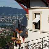 Belle Epoche über den Dächern von Zürich: Zipfelmützenzwerge und beflügelte Dämonen tragen an der alten Schlossfassade Teile der hölzernen Dachkonstruktion