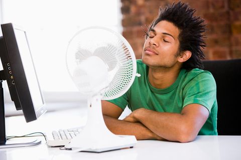 Hitze im Büro: Ein mann sitzt vor einem Ventilator