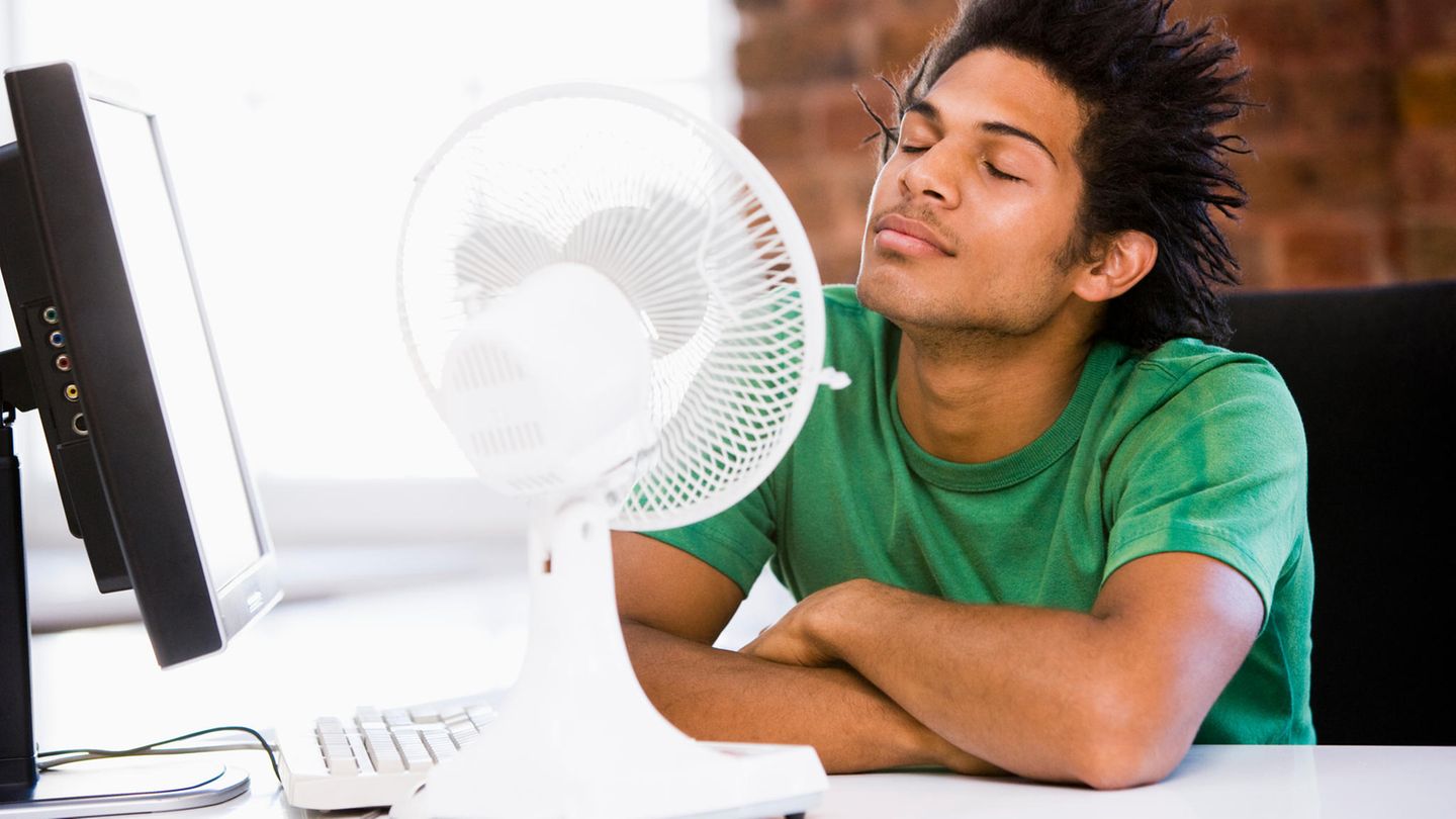 Hitze im Büro: Ein mann sitzt vor einem Ventilator