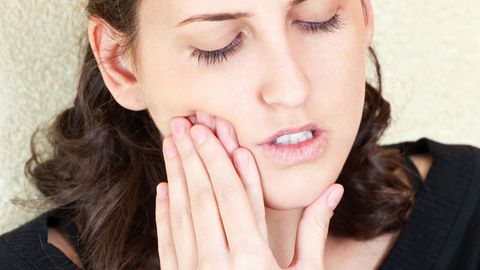 Zahnschmerzen: Eine Frau hält sich die Wange