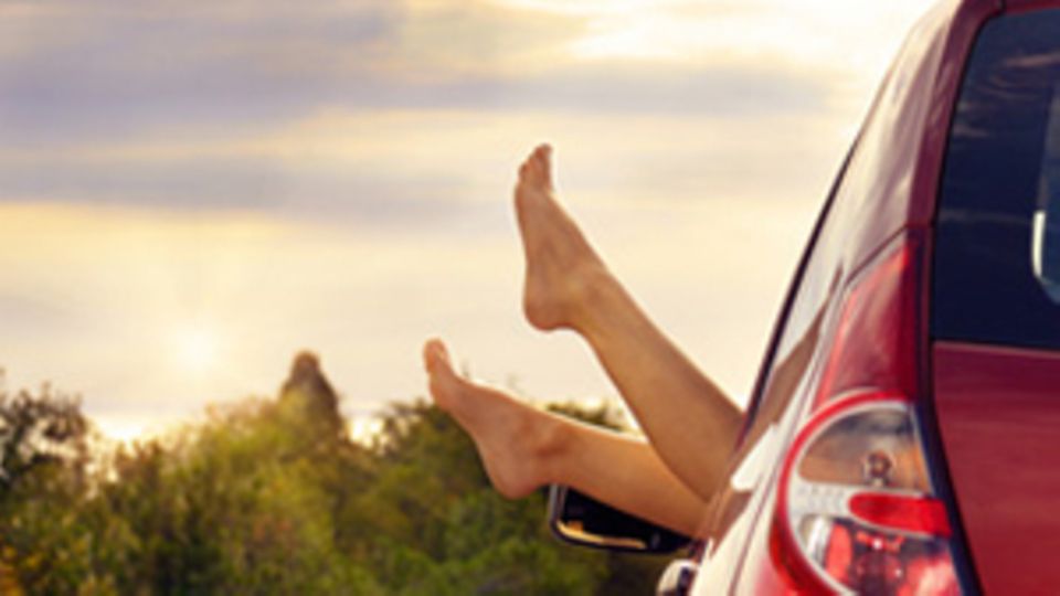 Nackte Füße werden aus dem offenen Fenster eines Autos gestreckt.