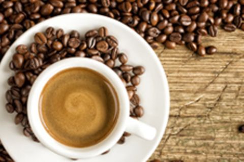 Eine Kaffeetasse um die Kaffeebohnen verstreut sind.