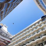 Die Perspektive des riesigen Patios im Heck auf Deck 6 zeigt die diagonale Seilrutsche mit einer über dem Abgrund schwebenden Person - eine der unendlichen vielen Freizeitmöglichkeiten von Kletterwänden bis zum Schlittschuhlaufen an Bord.