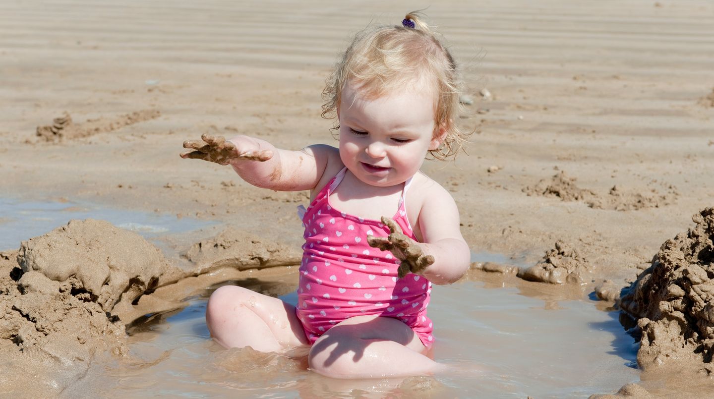 Ein Kind spielt im Sand - und zwar mit vollem Körpereinsatz