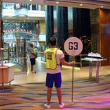 Auf Deck 5 und 6 ziehen sich Boardwalk und Royal Promenade mit Geschäften und Bars wie eine Shopping Mall durch das Längsschiff. Hier ein Bild von der Rettungsübung, die bereits vor dem Auslaufen des Schiffs absolviert wird. Auf meiner Chipkarte, die meine Kabinentür öffnet und gleichzeitig als Zahlungsmittel dient, ist zwar der Ort des Notfall-Sammelplatzes mit G3 größer markiert als die Kabinennummer. Allerdings bleibt mir die Seenotübung ein Rätsel. Während der halben Stunde des Rumstehens lerne ich viele Mitreisende kennen, doch wo sich meine Schwimmweste für den "unlikely event of an emergency" befindet, wird mir nicht verraten. Lautes Wassergeplätscher von einem Indoor-Springbrunnen übertönt die Durchsagen der Crew.