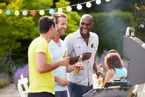 Männer stehen lachend um einen Grill herum