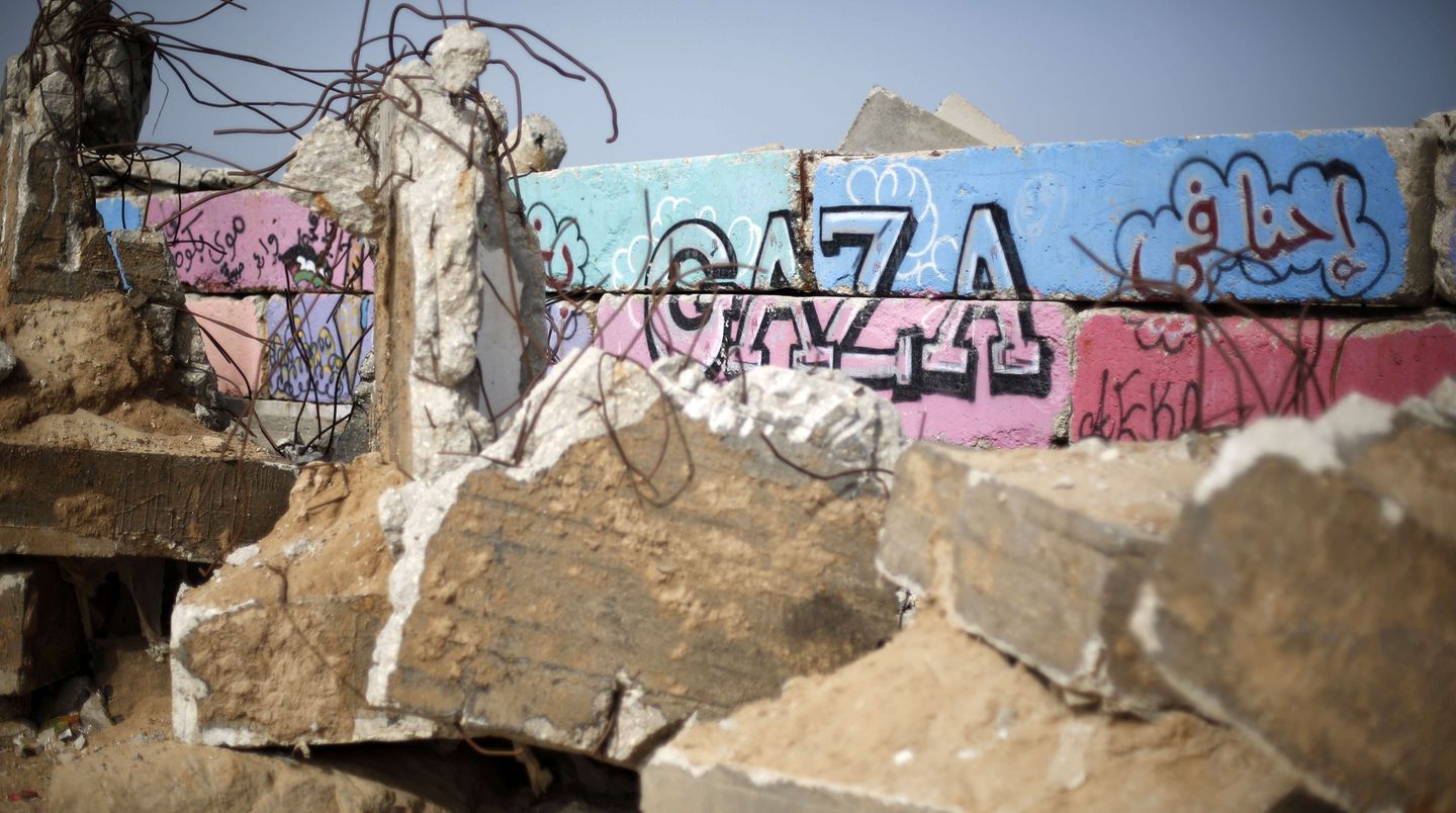 Trümmer liegen vor einer Mauer mit einem "Gaza"-Grafitto