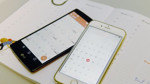 Ein iPhone und ein Android-Smartphone liegen mit geöffneter Kalender-App auf einem Papier-Planer