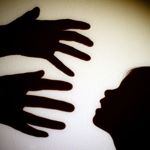 Schatten von Händen einer erwachsenen Person und dem Kopf eines Kindes an einer Wand eines Zimmers