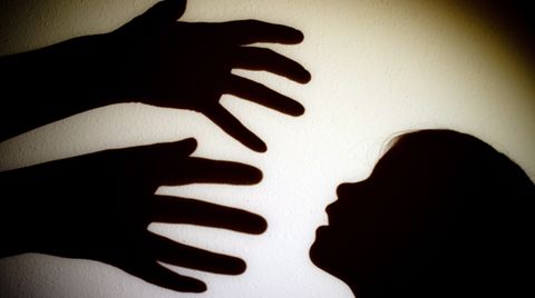 Schatten von Händen einer erwachsenen Person und dem Kopf eines Kindes an einer Wand eines Zimmers