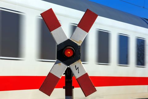 Ein rotes Warnsignal in einem Andreaskreuz leuchtet während ein Zug vorbei rast