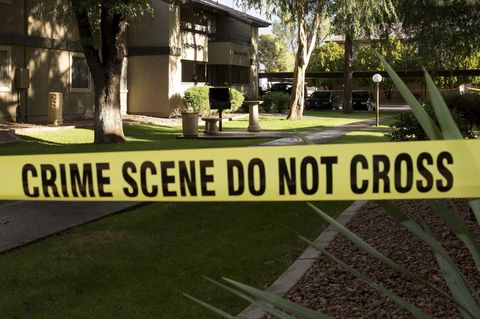Ein gelbes Polizei-Absperrband mit dem Schriftzug "Crime Scene Do not cross" vor einer Gartenanlage bei Sonnenschein