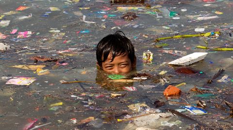 Ein Junge schwimmt in Manila in Wasser voller Müll