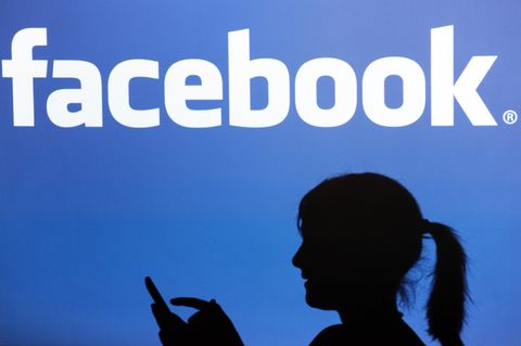 Vor dem Facebook-Logo ist der Schatten einer Frau zu sehen.