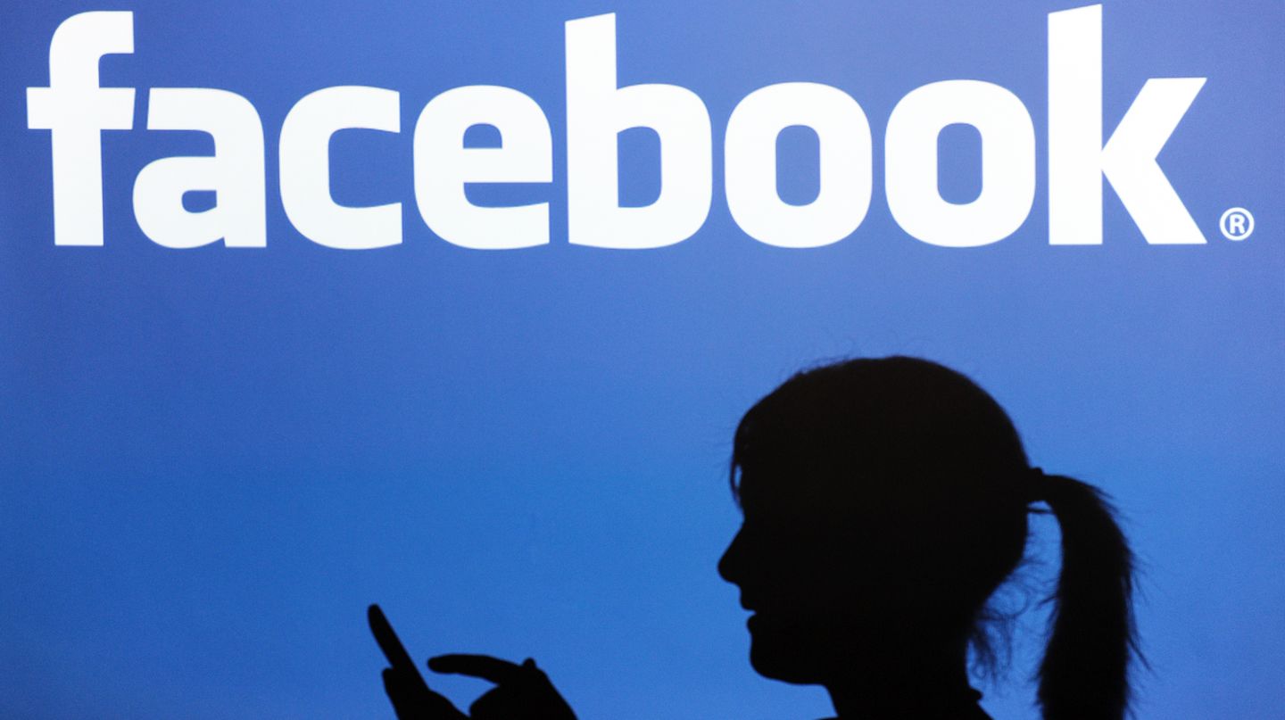 Vor dem Facebook-Logo ist der Schatten einer Frau zu sehen.