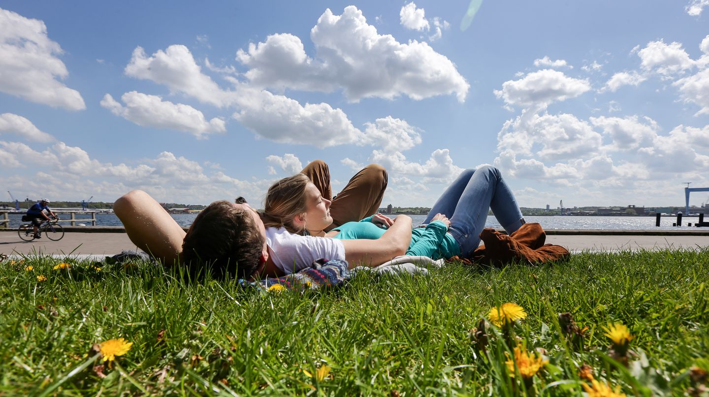 Ein Pärchen genießt auf einer Wiese in Kiel die wärmende Sonne