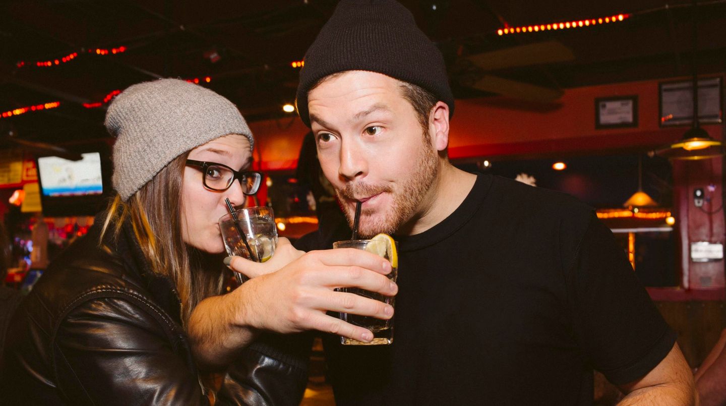 Zwei junge Menschen stehen in einer Bar und trinken Alkohol