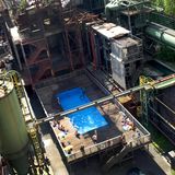 Es ist das wohl ungewöhnlichste Freibad Deutschlands: das Werksschwimmbad der Zeche Zollverein in Essen, das mitten in die Reste der ehemaligen Kokerei montiert wurde. Für den Badespaß haben Frankfurter Künstler zwei Überseecontainer aneinandergeschweißt und auf ein Holzgestell gesetzt. Das dient nun als Liegewiese.