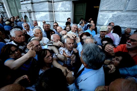 Ein Mitarbeiter der National Bank of Greece wird von Rentnern überwältigt, als er Wartenummern für die Geldschalter verteilt