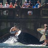 Eine coole Möglichkeit, sich in München abzukühlen: Surfen auf der Eisbachwelle. Wie immer an heißen Tagen stehen die Wellenreiter Schlange im Englischen Garten. Doch die Juli-Hitze hinterlässt auch hier ihre Spuren: Das sonst so eisige Bächlein hat sich inzwischen bereits auf Wassertemperaturen von über 17 Grad aufgewärmt.