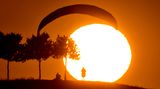 Freizeitsportler warten bei der derzeitigen Hitze besser bis in die Abendstunden, ehe sie joggen, radeln - oder eben paragleiten. Dieser Gleitschirmflieger übt am Kronsberg in Hannover beim Sonnenuntergang das sogenannte Groundhandling, die Kontrolle des Schirms am Boden.