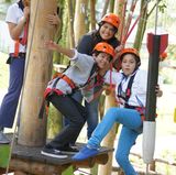 Im Hochseilgarten Hanserock in Hamburg lachen drei Kinder auf einer hölzernen Plattform.