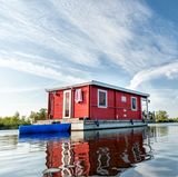 Ein rotes Hausboot schwimmt auf einem See in Brandenburg