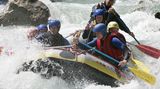 Männer und Frauen machen Rafting auf einem Wildwasser-Fluss in den Alpen