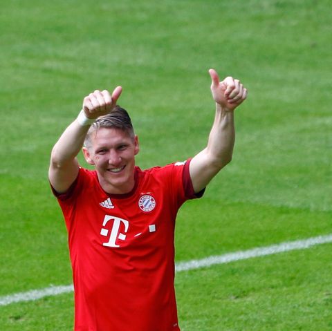 Bastian Schweinsteiger im roten FC Bayern Trikot hält auf dem Fußballplatz grinsend seine Daumen in die Luft