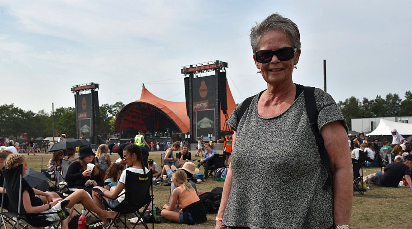 Roskilde Festival 2015: Anne-Grethe (68) ist seit Anfang an dabei. 44 Jahre haben sie und ihre Familie ehrenamtlich auf dem Roskilde Festival gearbeitet. Während ihre Mutter mit stolzen 72 Jahren dem Festival den Rücken zu wandte will sie weitermachen bis sie 74 wird. Das erste noch "kommerzielle" Fantasy Festival im Jahre 1971 hatte sie noch ausgelassen. Zwei Schüler aus dem Ort wollten damals "ihre" Musik nach Seeland bringen, doch ihr Kopenhagener Kompagnon brannte mit der Kasse durch. Im darauf folgenden Jahr begann die Geschichte des eigentlichen Roskilde Festivals. Zunächst als Versuch das örtliche – ebenfalls in die roten Zahlen geratene – Volksfest zu retten. Da war die damals vierundzwanzigjährige Anne-Grethe schon mit von der Partie. Anne-Grethe (68) ist seit Anfang an dabei. 44 Jahre haben sie und ihre Familie ehrenamtlich auf dem Roskilde Festival gearbeitet. Während ihre Mutter mit stolzen 72 Jahren dem Festival den Rücken zu wandte will sie weitermachen bis sie 74 wird. Das erste noch "kommerzielle" Fantasy Festival im Jahre 1971 hatte sie noch ausgelassen. Zwei Schüler aus dem Ort wollten damals "ihre" Musik nach Seeland bringen, doch ihr Kopenhagener Kompagnon brannte mit der Kasse durch. Im darauf folgenden Jahr begann die Geschichte des eigentlichen Roskilde Festivals. Zunächst als Versuch das örtliche – ebenfalls in die roten Zahlen geratene – Volksfest zu retten. Da war die damals vierundzwanzigjährige Anne-Grethe schon mit von der Partie.